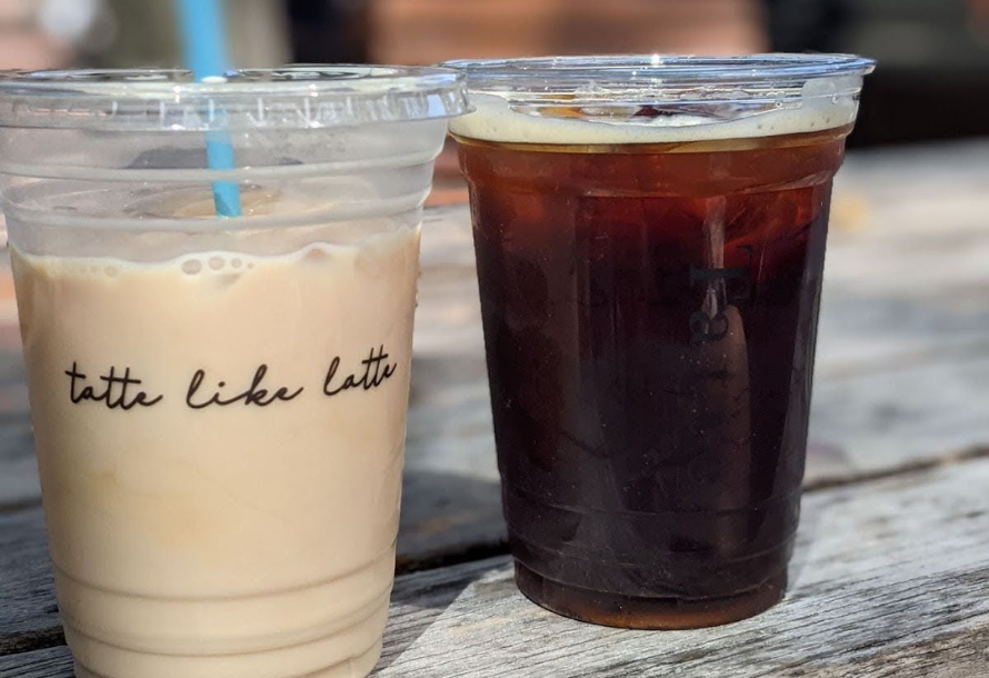 An iced coffee and a cold brew sitting next to each other on a picnic table
