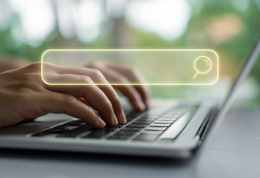 Person typing on a laptop. Search bar graphic overlay on top of photo.