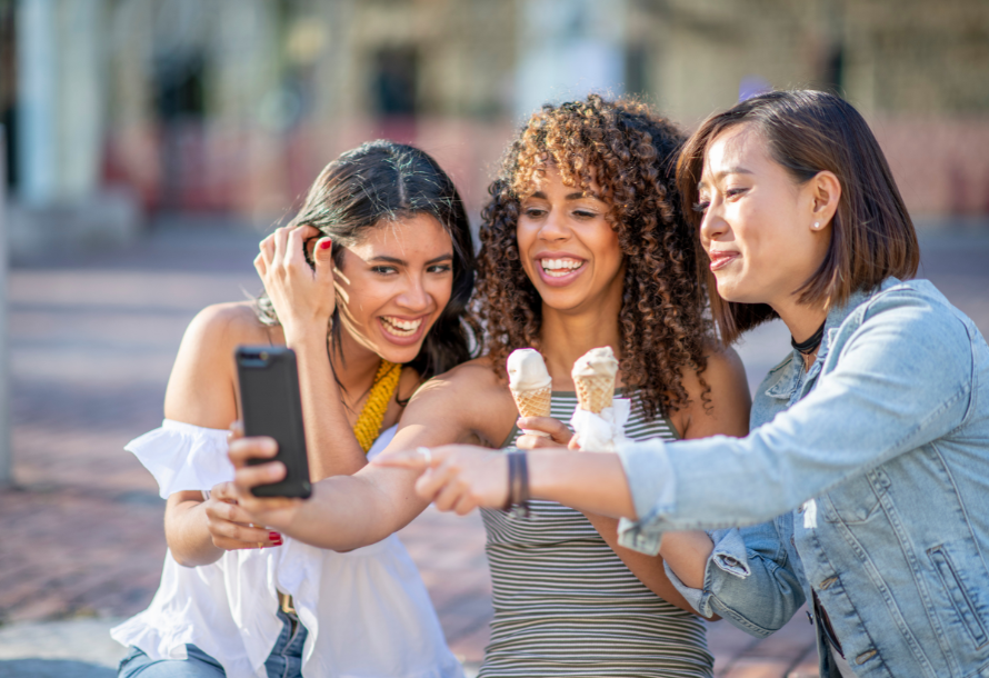 Three women enjoying ice cream cones while taking a selfie.