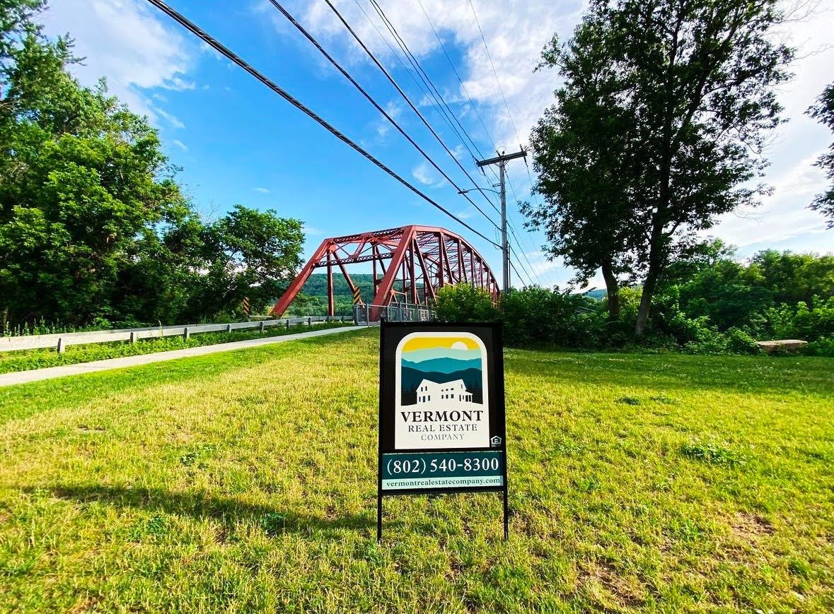 Vermont Real Estate Company sign on a grassy landscape in front of a bridge.