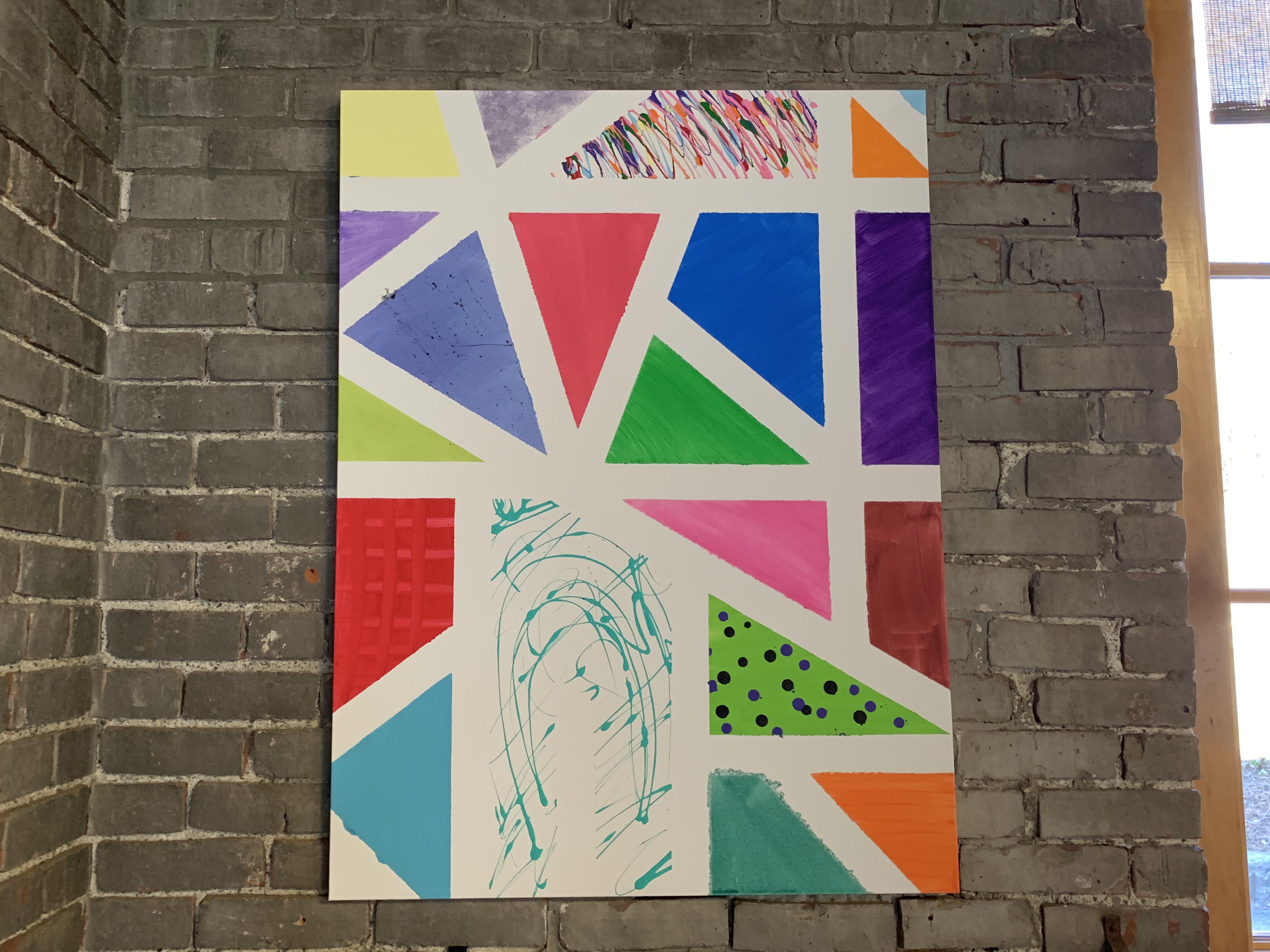 An abstract, colorful painting against a gray brick wall.