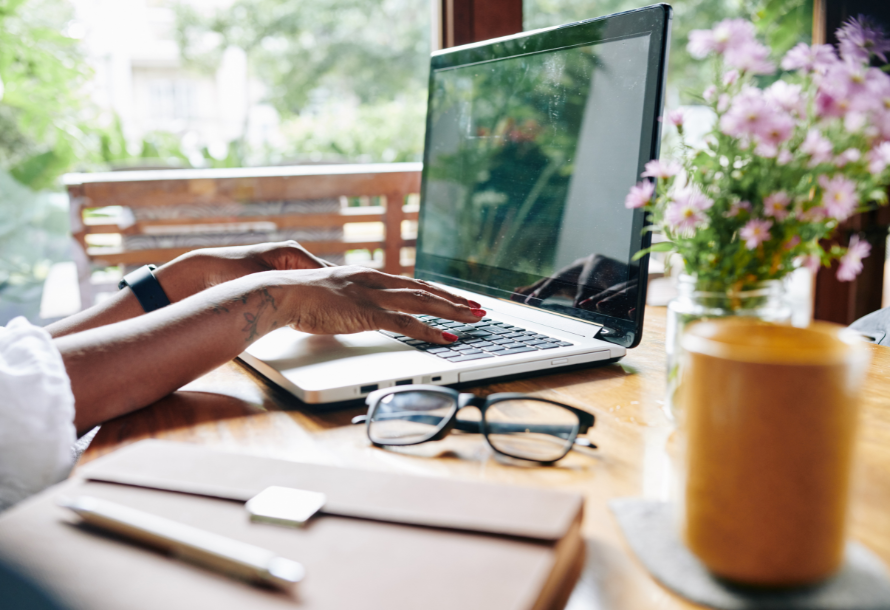 Person typing on a laptop with a floral plant by their side.